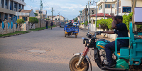 A man riding a motorcycle with a delivery cart down a street. Photo by Ato Aikins on Unsplash