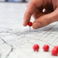 A hand placing red push pins into city street map.. Photo by GeoJango Maps on Unsplash