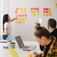 Woman placing sticky notes on wall. Photo by Jason Goodman on Unsplash